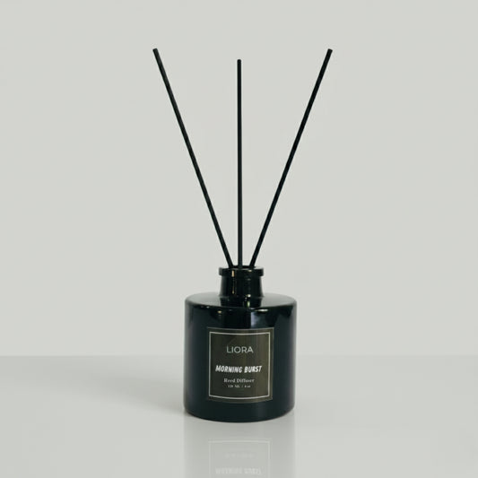 Liora Scentique Morning Burst reed diffuser in a black glass bottle with black reeds, photographed against a clean light grey studio background.