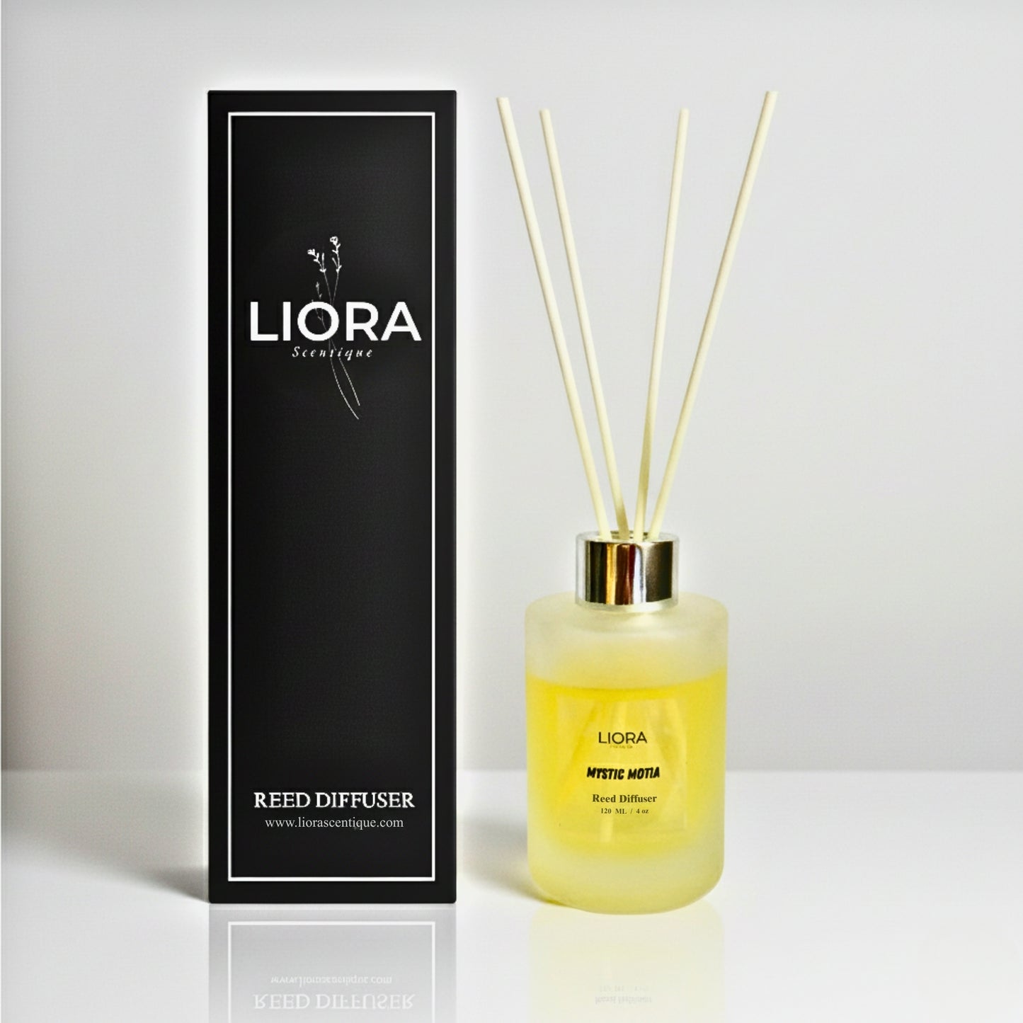 Liora Scentique Mystic Motia reed diffuser on a marble table with white jasmine flowers and soft natural light, showcasing the white reeds and frosted glass bottle.