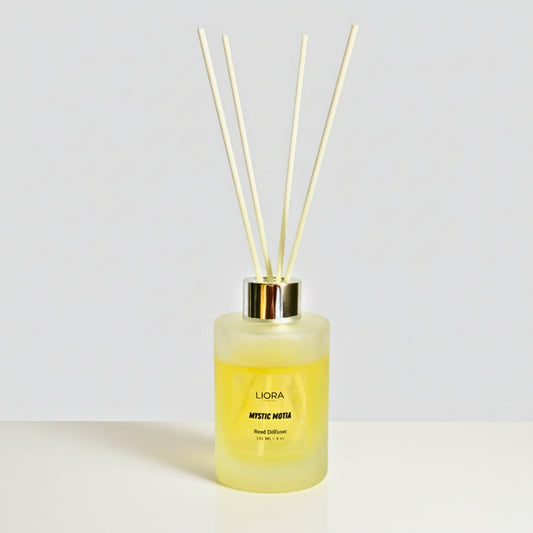 Liora Scentique Mystic Motia reed diffuser on a marble table with white jasmine flowers and soft natural light, showcasing the white reeds and frosted glass bottle.