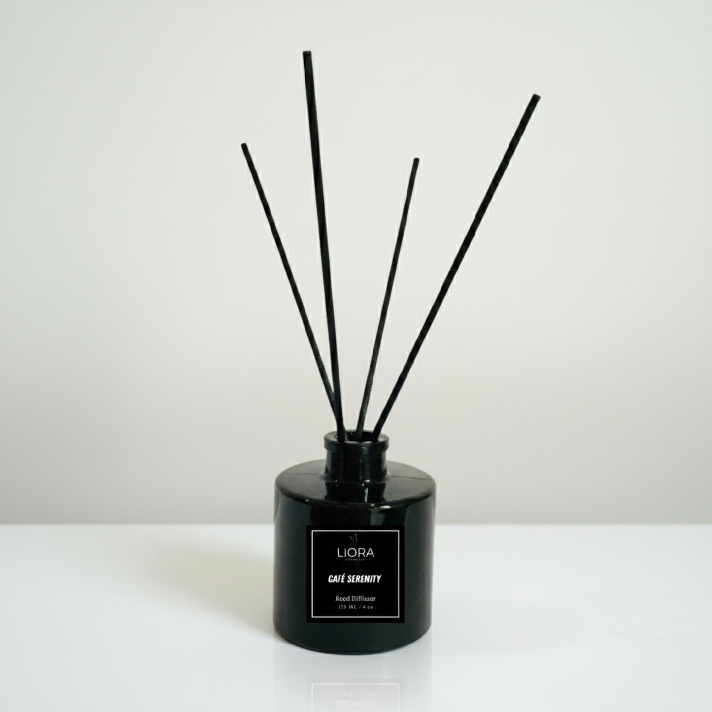 Liora Scentique Café Serenity reed diffuser in a black glass bottle with black reeds, photographed against a clean light grey studio background.