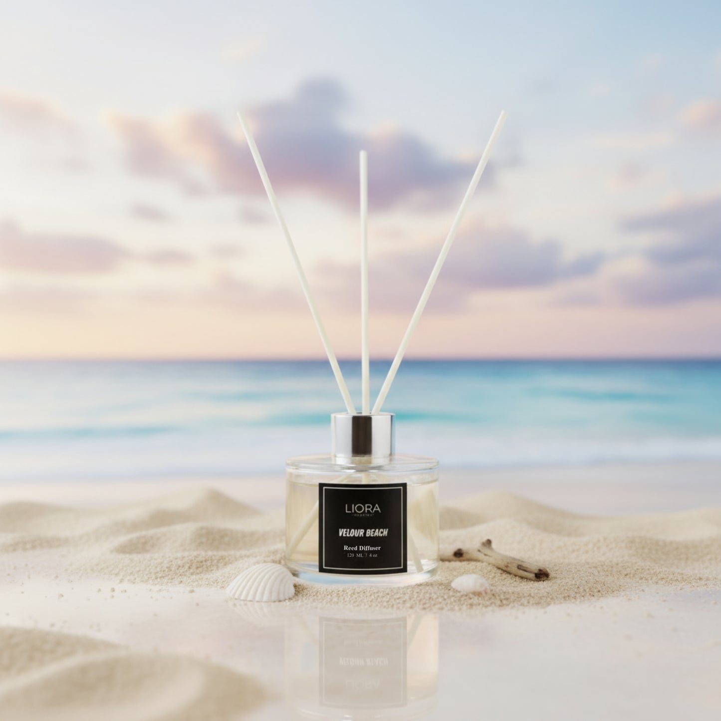 Liora Scentique Velour Beach reed diffuser with white reeds on driftwood, shells, and lavender, with the ocean and beach in the background.