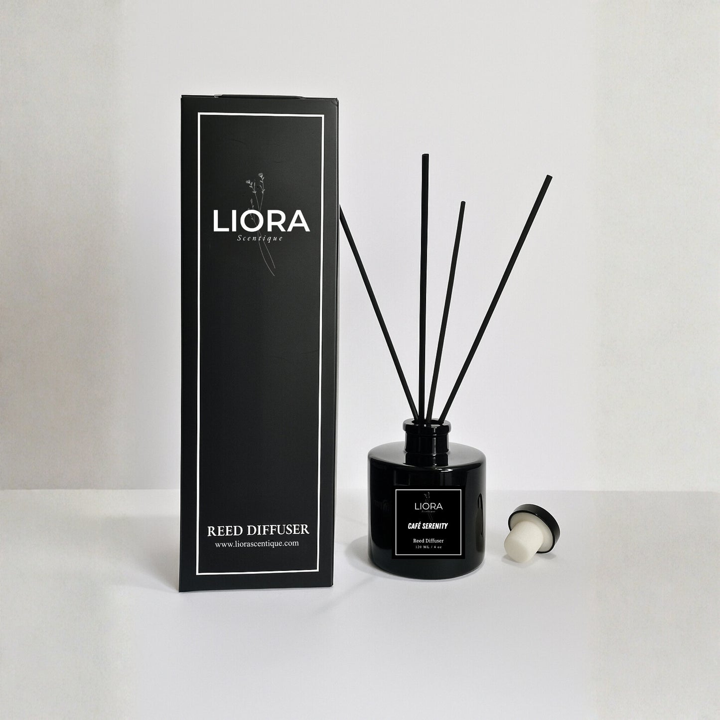 Liora Scentique Café Serenity reed diffuser in a black glass bottle with black reeds, photographed against a clean light grey studio background.