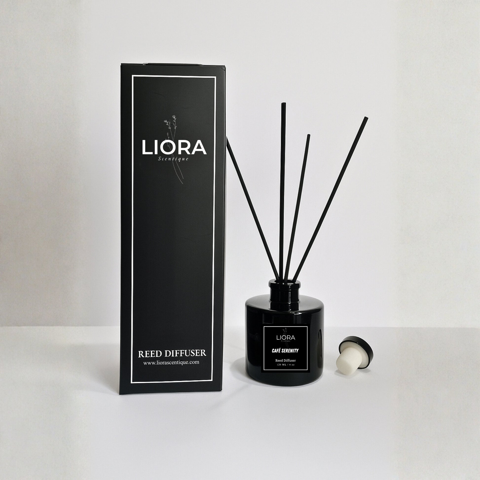 Liora Scentique Café Serenity reed diffuser in a black glass bottle with black reeds, photographed against a clean light grey studio background.